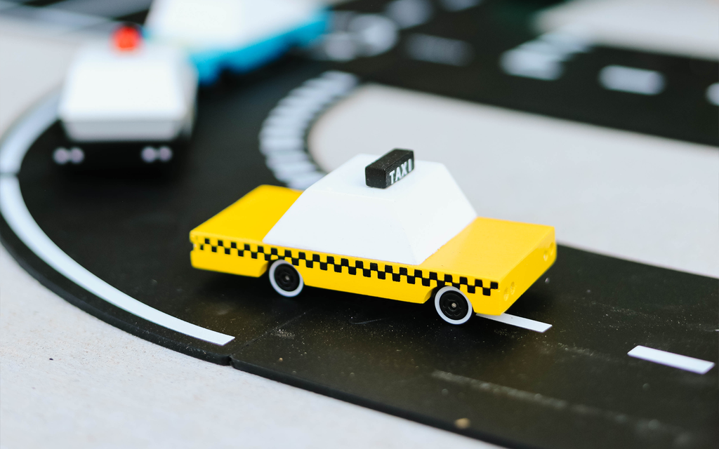 Toy taxi on a track with other toy vehicles in the background