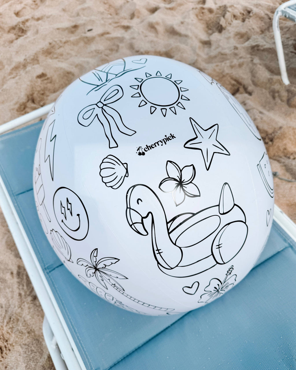 Beach ball with black line drawings on a blue chair at the beach