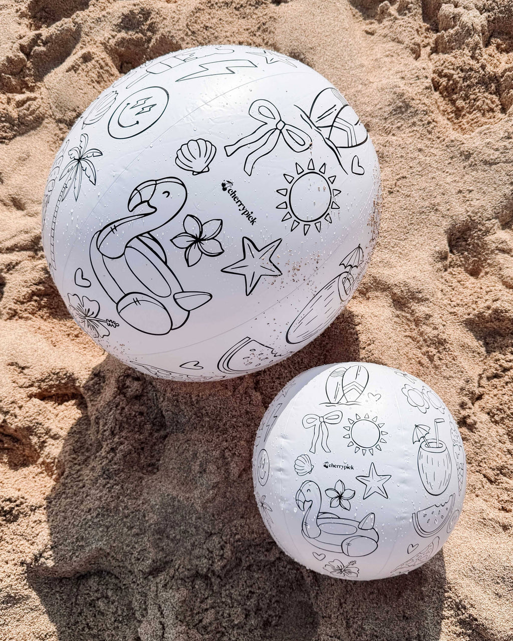 Two white balls with black line art designs on a sandy surface