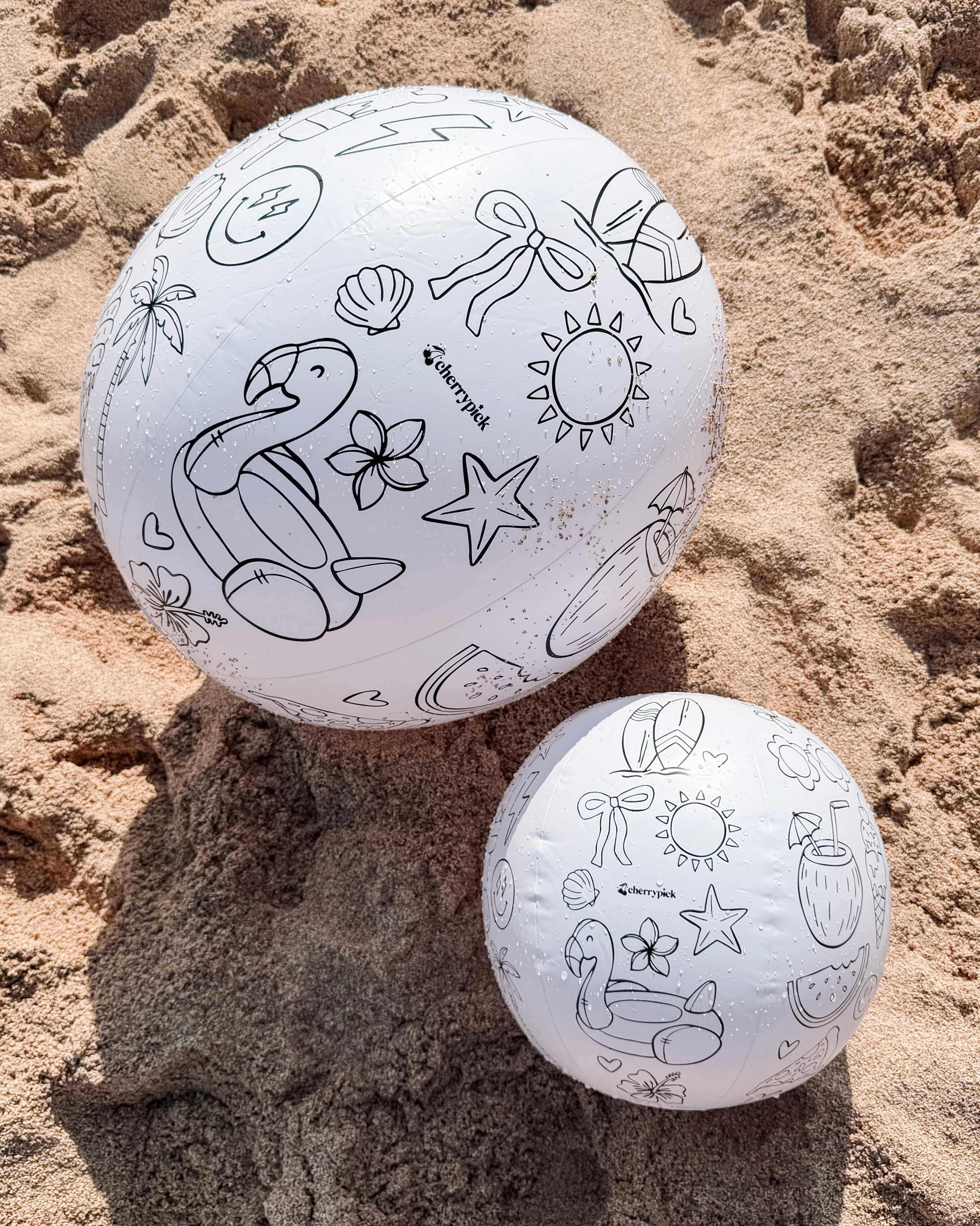 Two white balls with black line art designs on a sandy surface