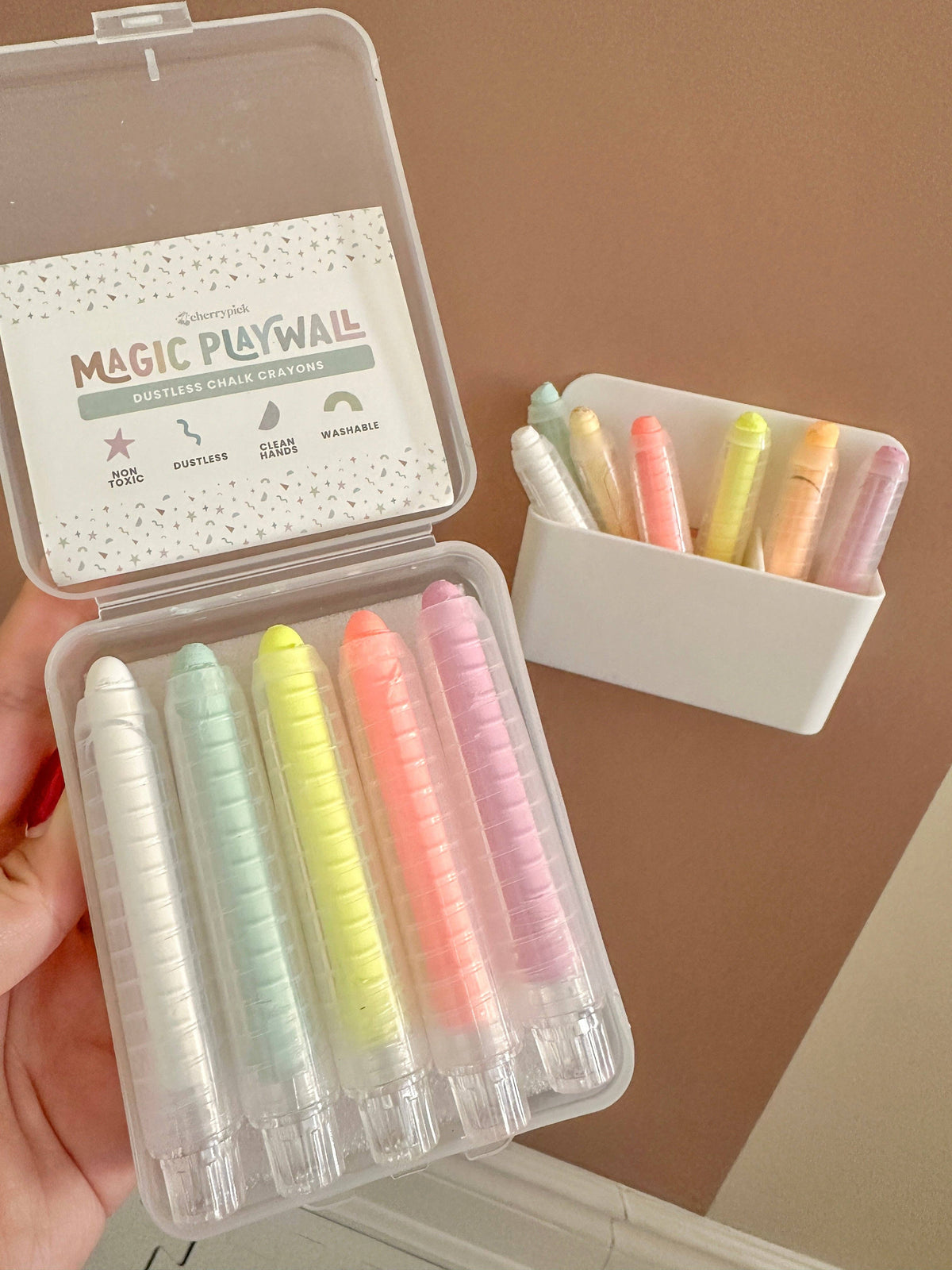 Set of colorful chalks in a transparent case with a small container of additional chalks on a brown background.