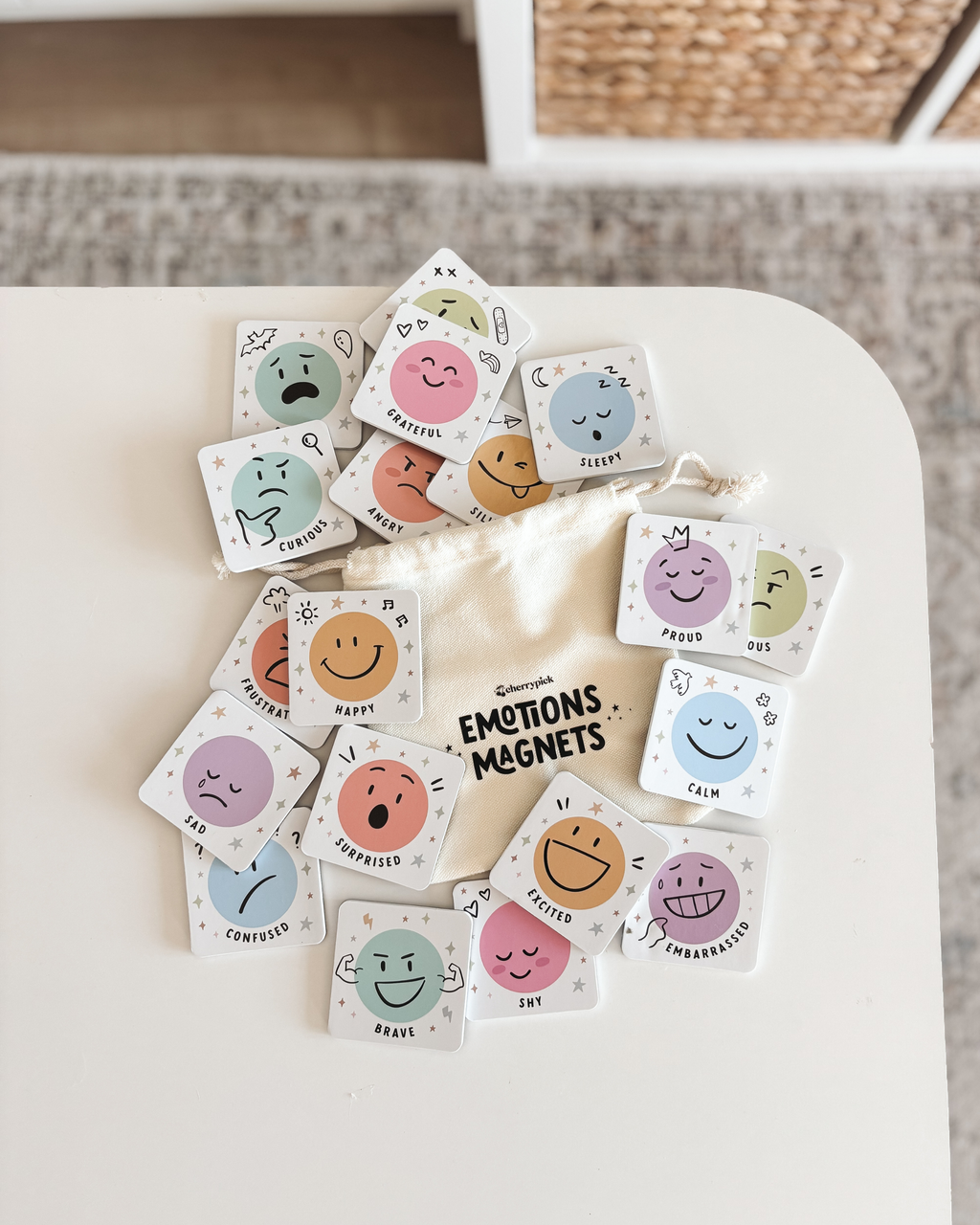An Emotions Magnets educational toy set by Cherrypick, featuring a white box surrounded by various small square magnets with colorful cartoon faces on a clean white background.