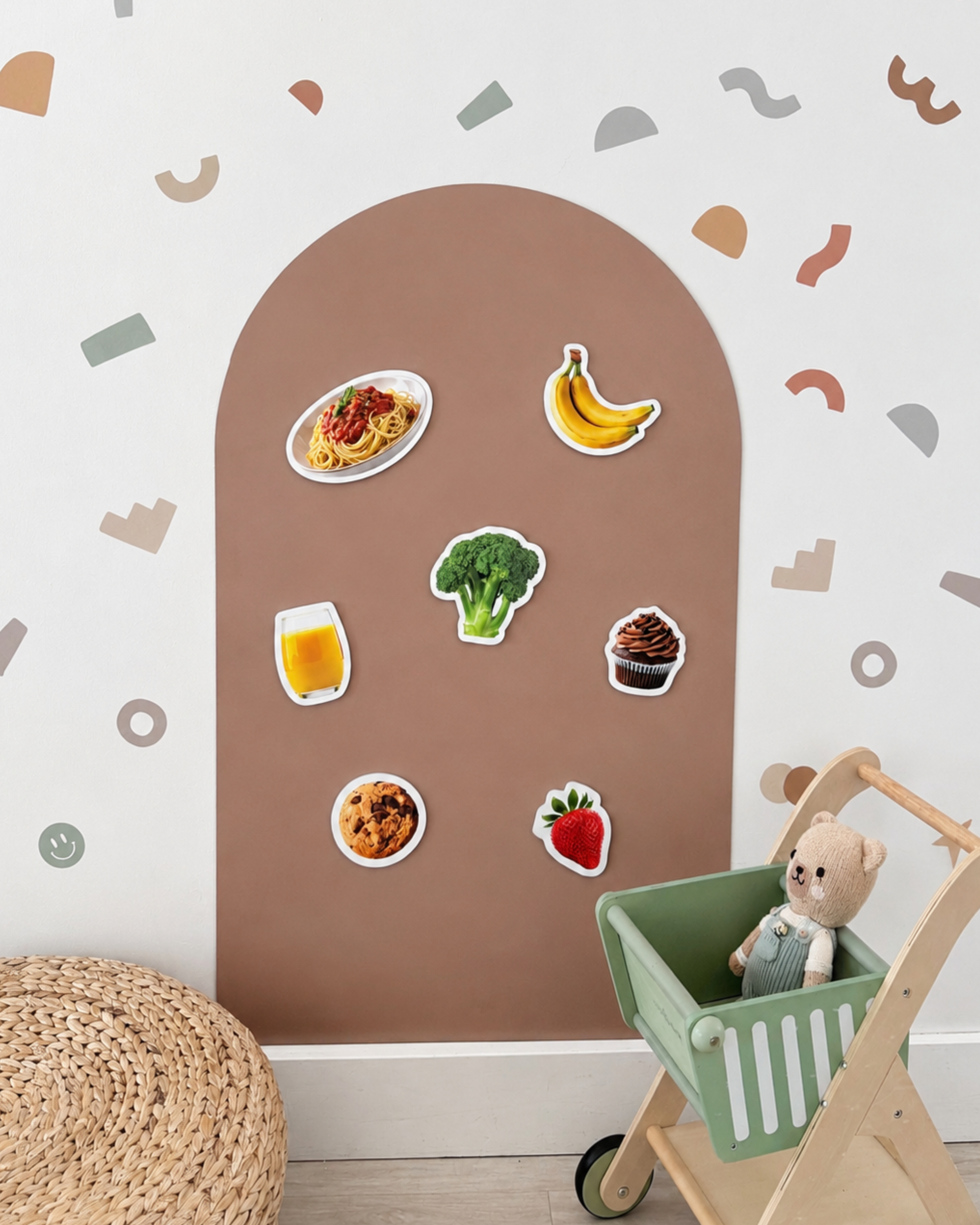 Wall with food-themed stickers and a toy trolley with a teddy bear.