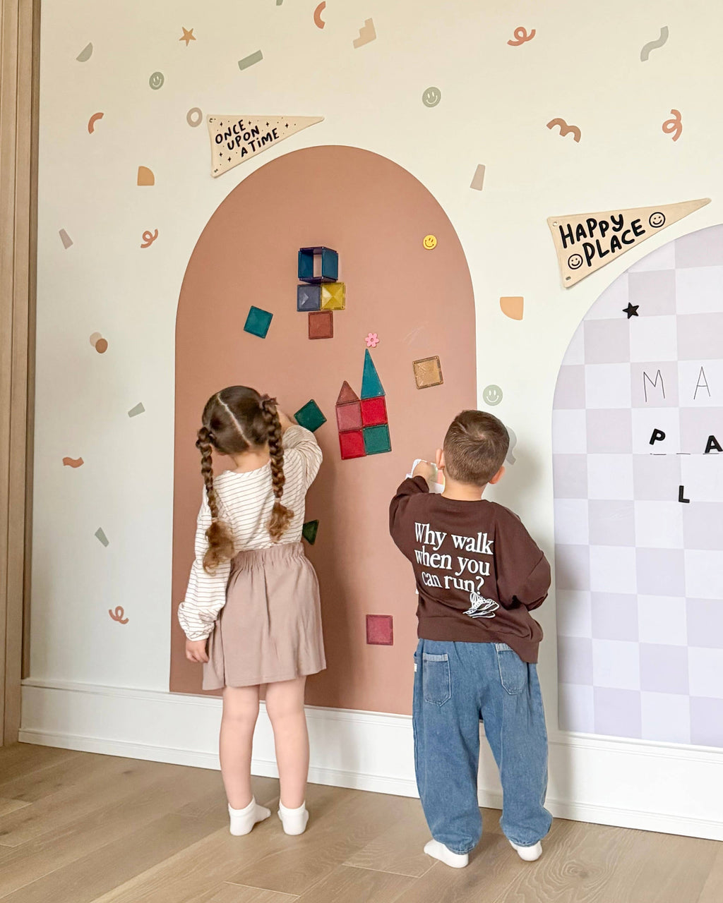 Two children playing with colorful magnetic letters on a decorative wall.
