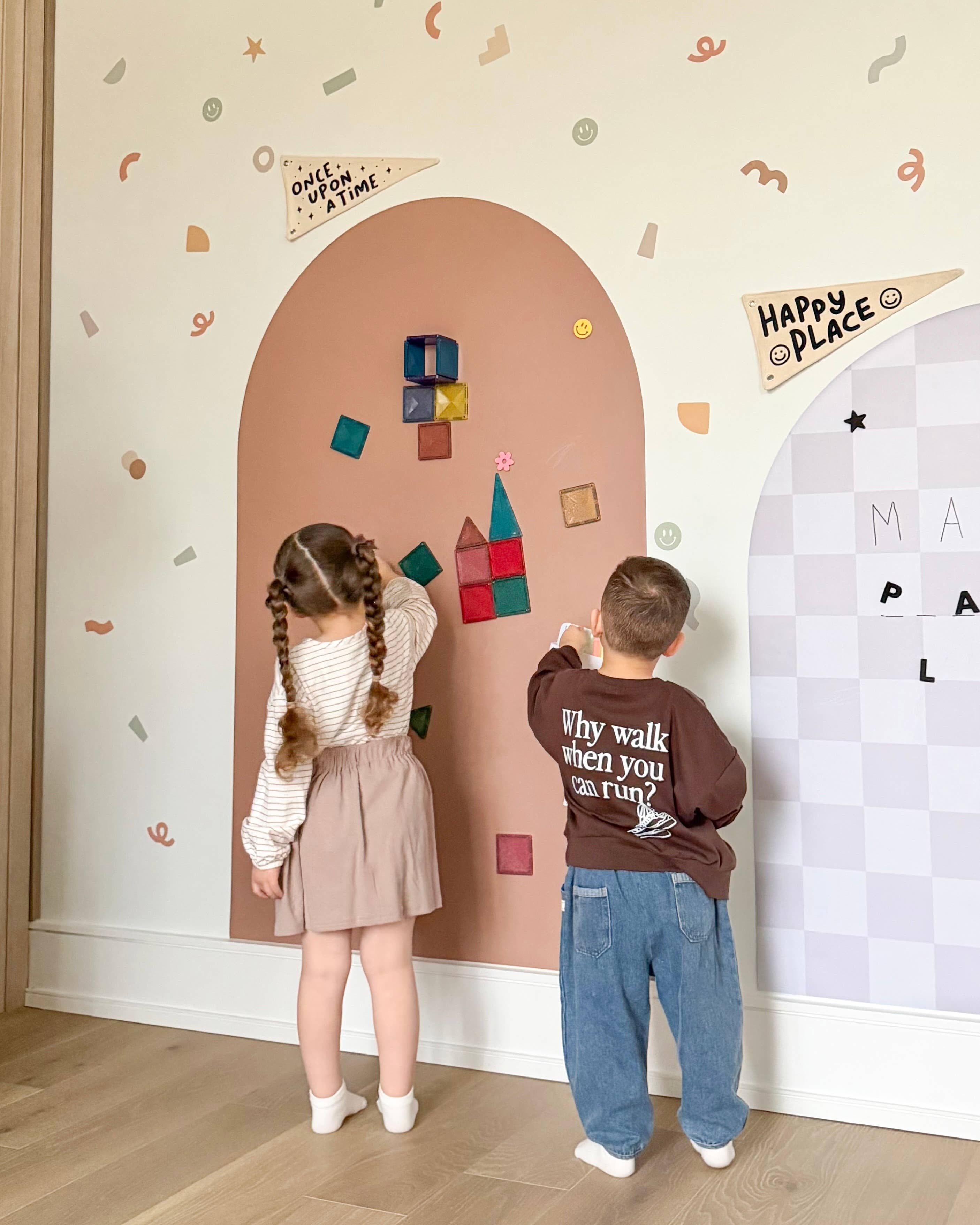 Two children playing with colorful magnetic letters on a decorative wall.