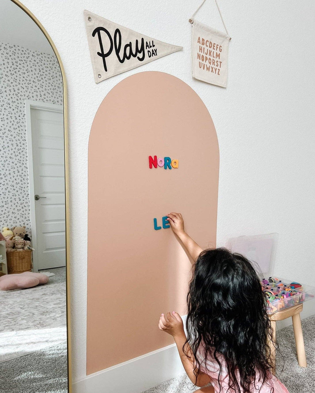 Child writing on a pink board with colorful letters in a room with decorative elements.
