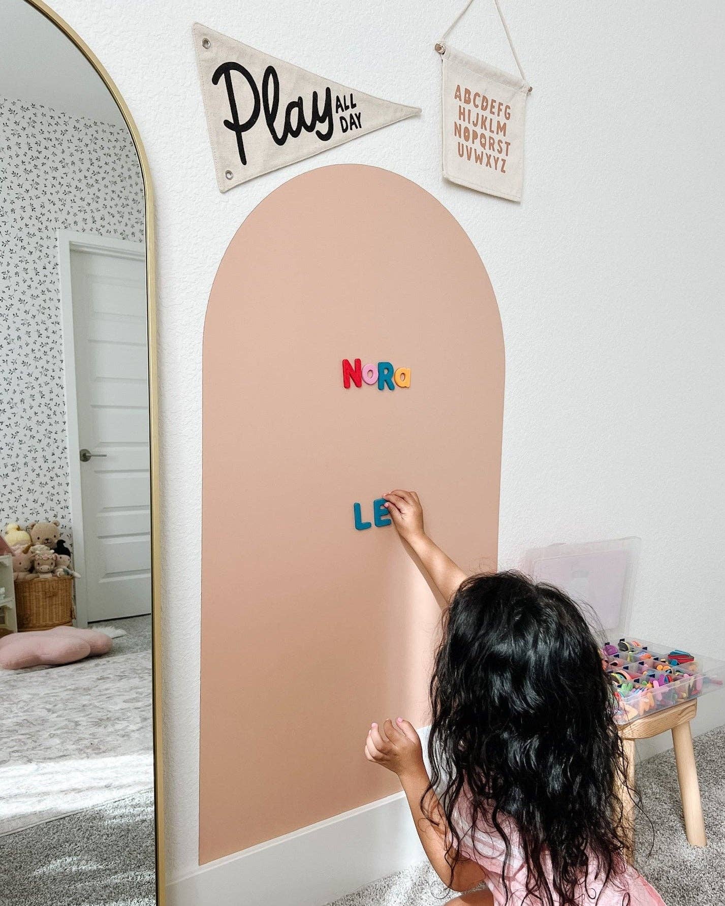 Child writing on a pink board with colorful letters in a room with decorative elements.