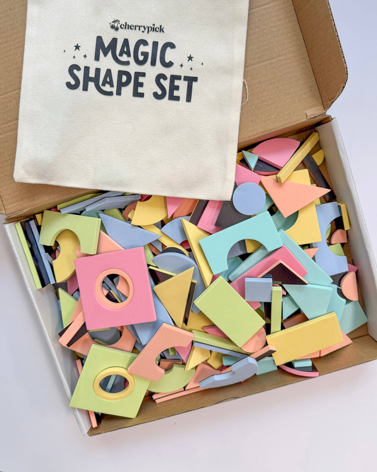 Colorful wooden shape set with a 'Cherry Pick' bag labeled 'Magic Shape Set' on a white background.