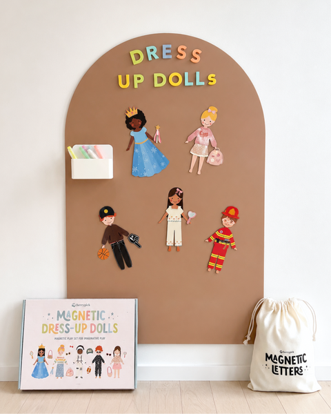 Dress-up dolls set with magnetic letters on a brown board, next to a box and drawstring bag.