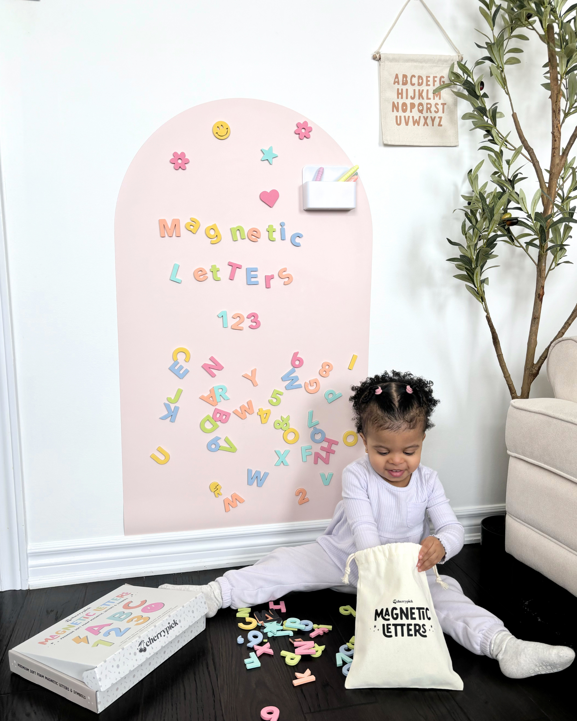 Child playing with magnetic letters in front of a pink board with more letters.