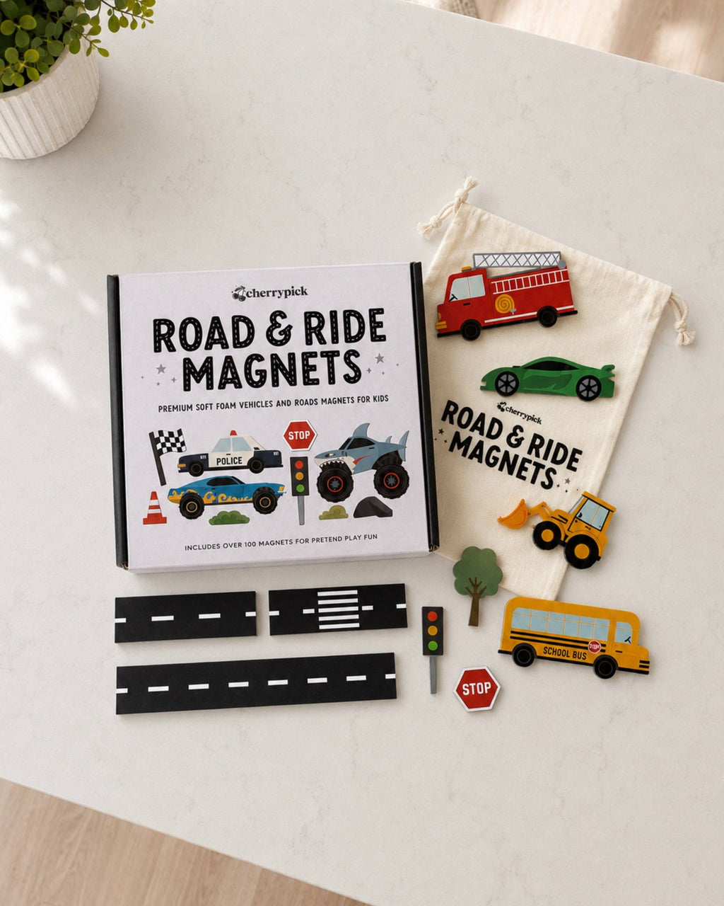 A children's road and ride magnets set by Chilly Pick, shown as a flat-lay on a white marble surface. The set includes a white book-style box with illustrations of vehicles, a cream drawstring bag, and multiple colorful magnets shaped like a fire truck, sports car, school bus, construction vehicle, trees, stop sign, and road sections.