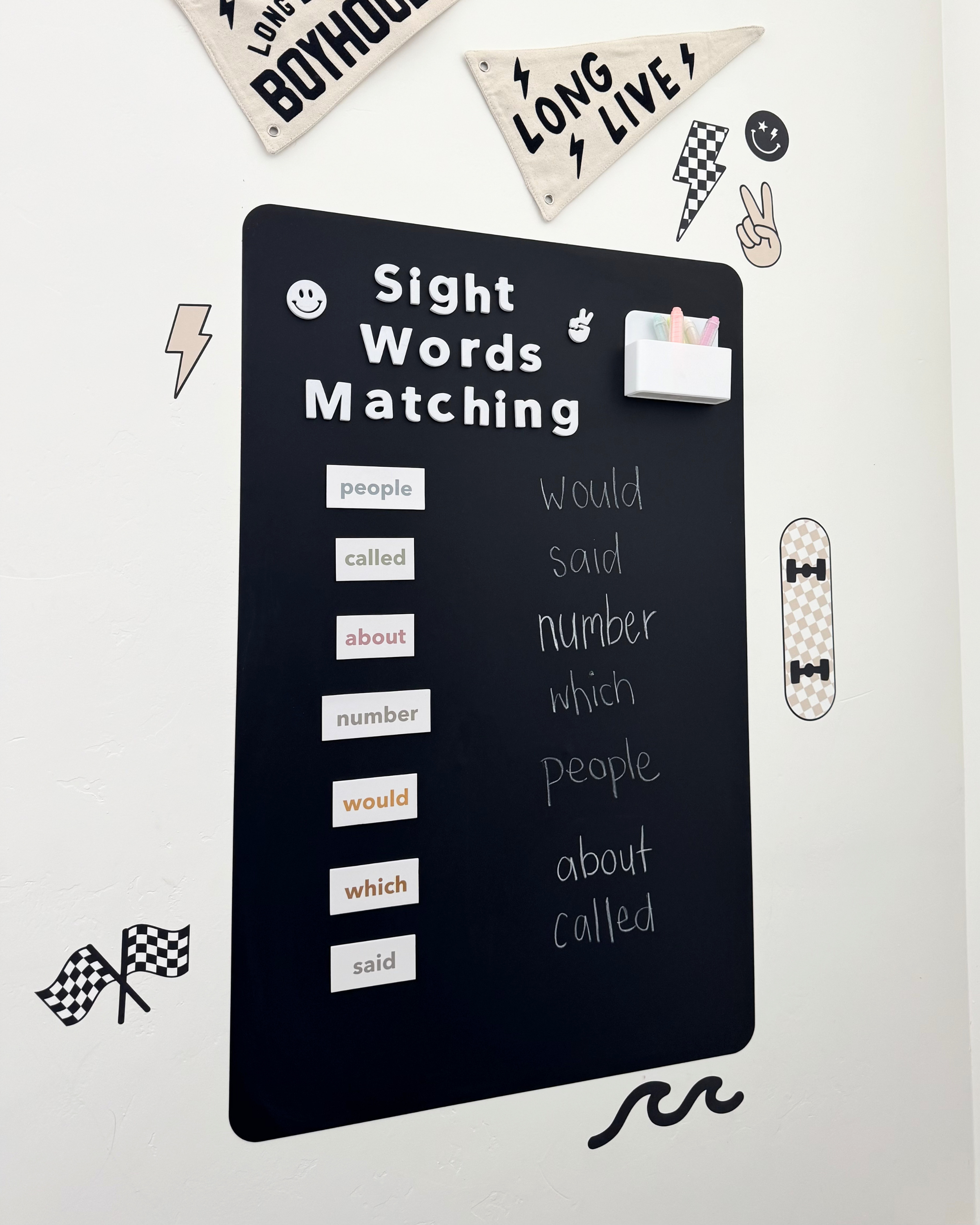 Black chalkboard with sight words matching activity on a white wall with decorative elements.