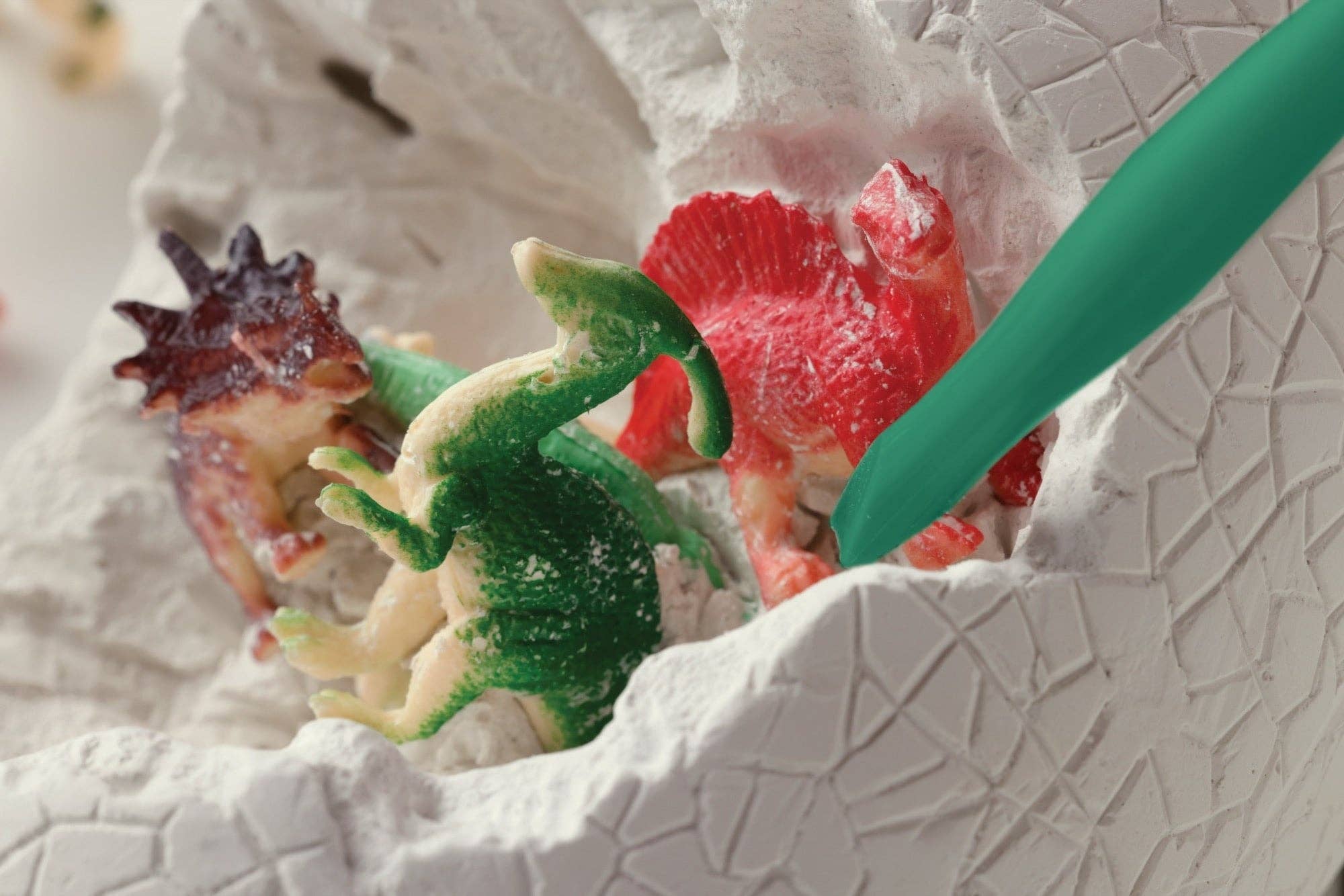 Colorful dinosaur toys in a textured white container with a green tool.