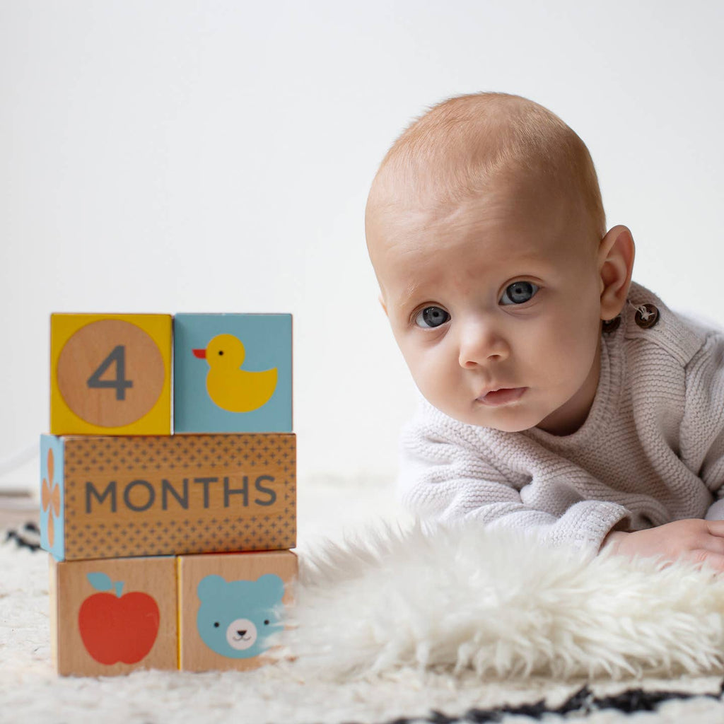 Baby with milestone blocks indicating 4 months, sitting on a white surface.