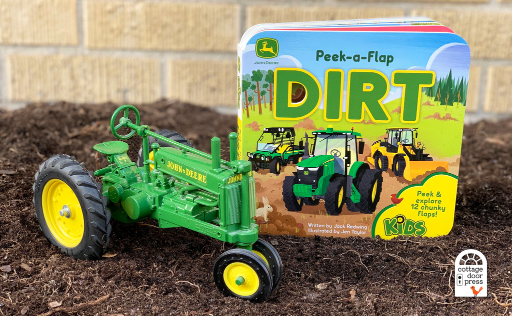 Toy tractor next to a children's book titled 'Peek-a-Flap Dirt' on a dirt surface.