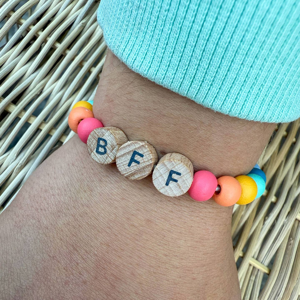 Colorful beaded bracelet with letter beads on a wrist, against a woven background.