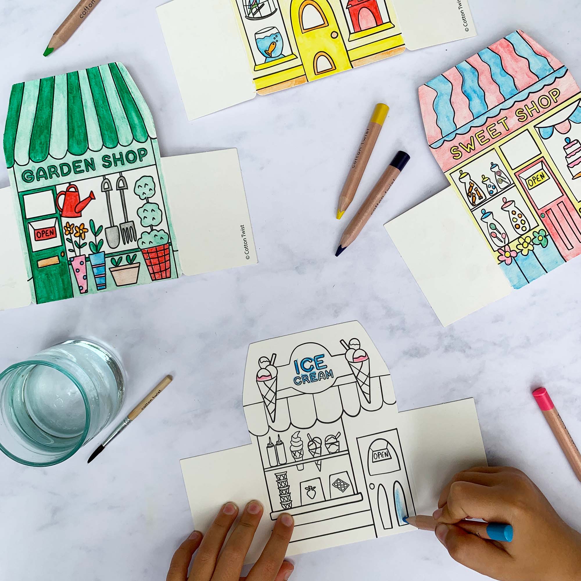 Coloring books with illustrations of shops on a table with coloring supplies.