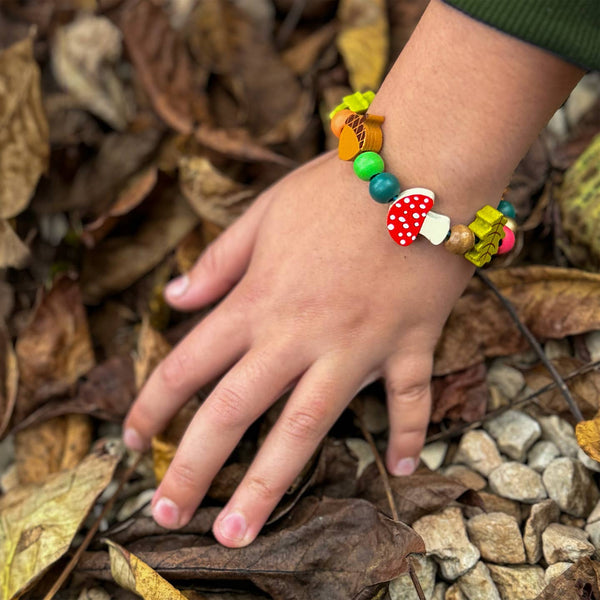 Colorful beaded bracelet on a child's wrist with a natural background of leaves and stones