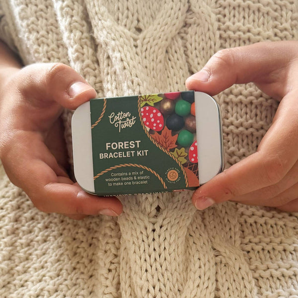 Forest bracelet kit packaging held by hands on a knitted fabric background