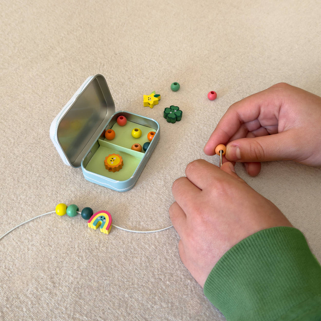 Person assembling colorful beads on a string next to an open tin with more beads.