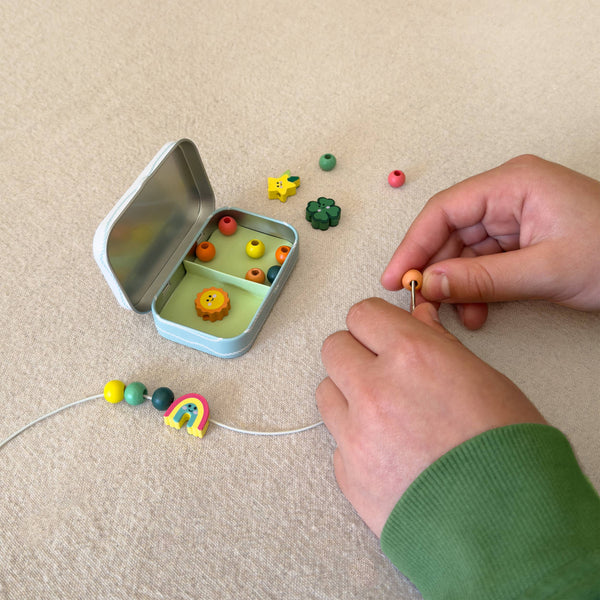 Person assembling colorful beads on a string next to an open tin with more beads.