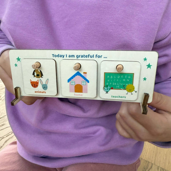 Child holding a gratitude board with illustrations and text on a purple shirt.