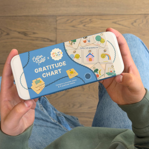 Person holding a 'Gratitude Chart' packaging on a wooden floor.