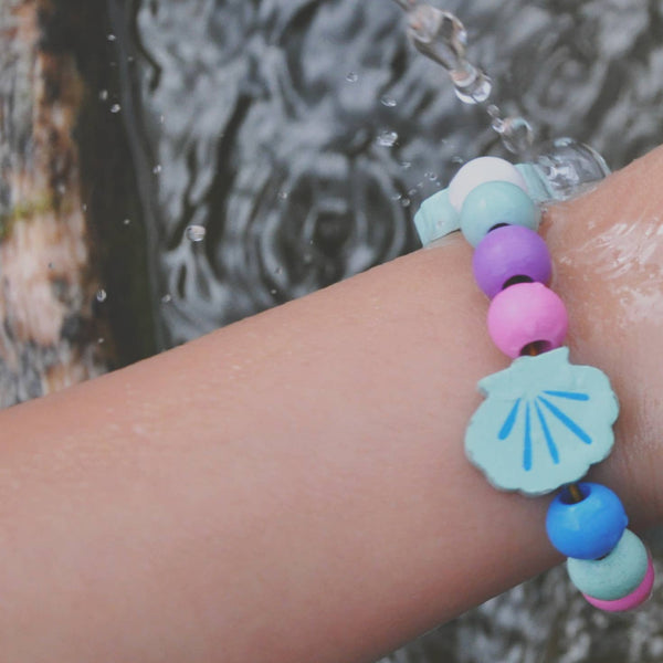 Colorful beaded bracelet with a shell charm on a wrist by a water source