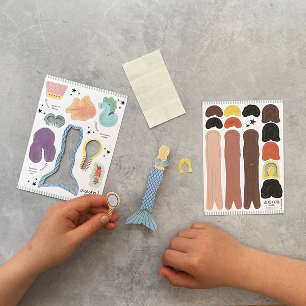 Children's hands interacting with a mermaid toy and color swatch on a gray surface