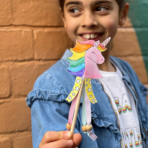 Child holding a colorful unicorn paper toy against a brick wall.