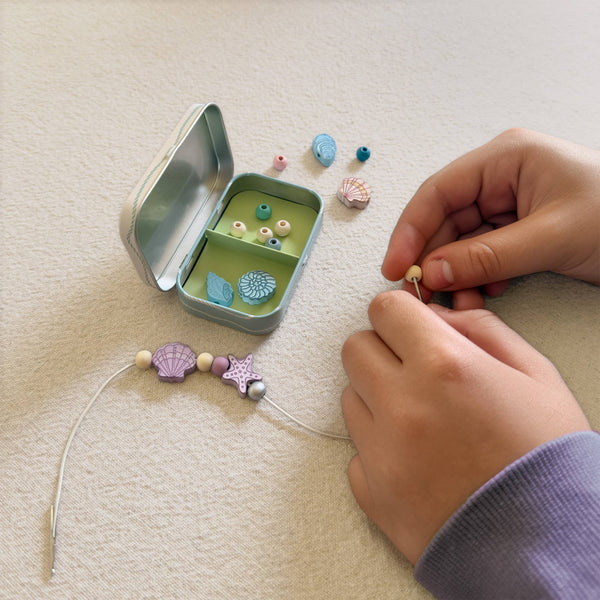 Child's hands working with beads and a small green box on a beige surface