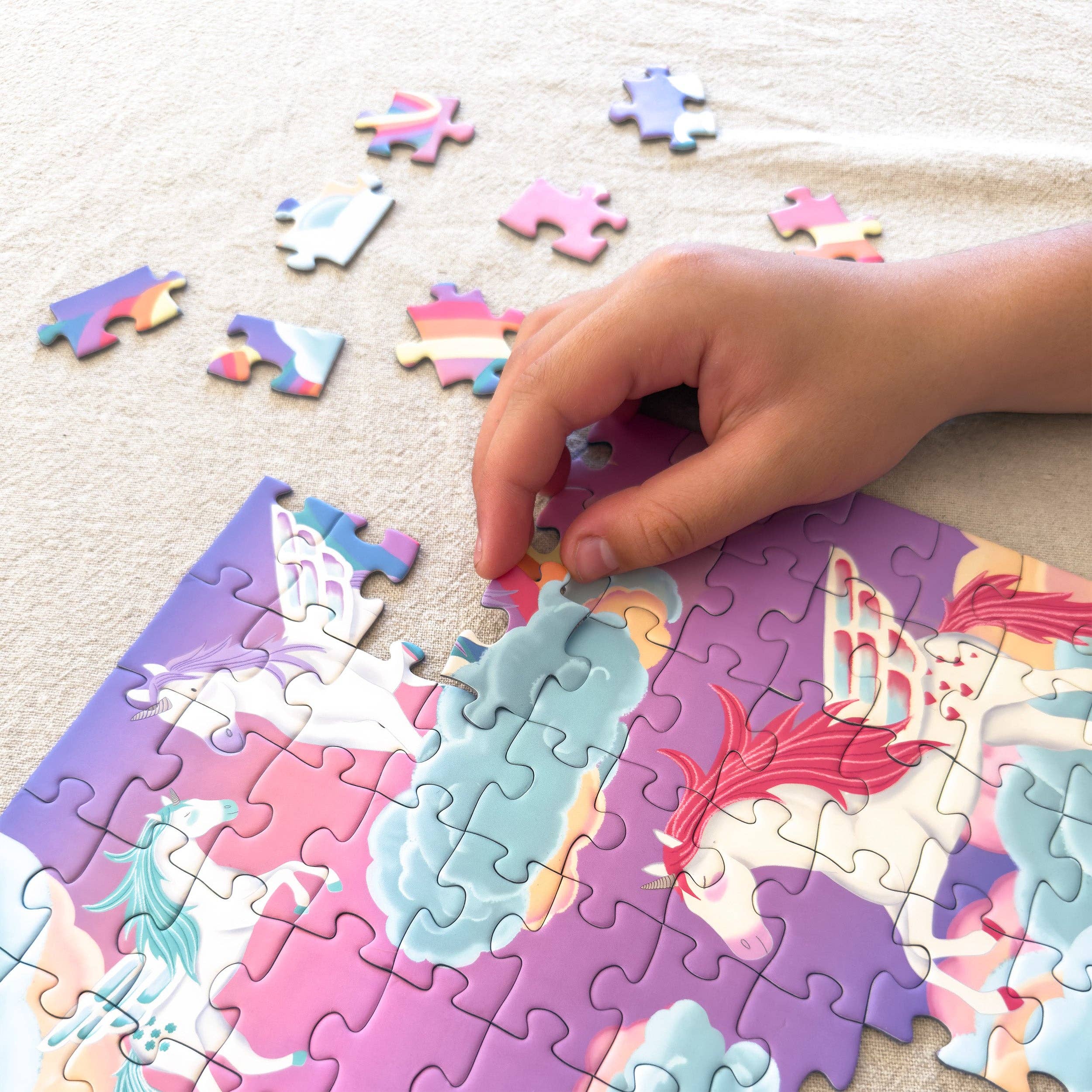 Child's hand placing a puzzle piece on a colorful unicorn-themed puzzle.