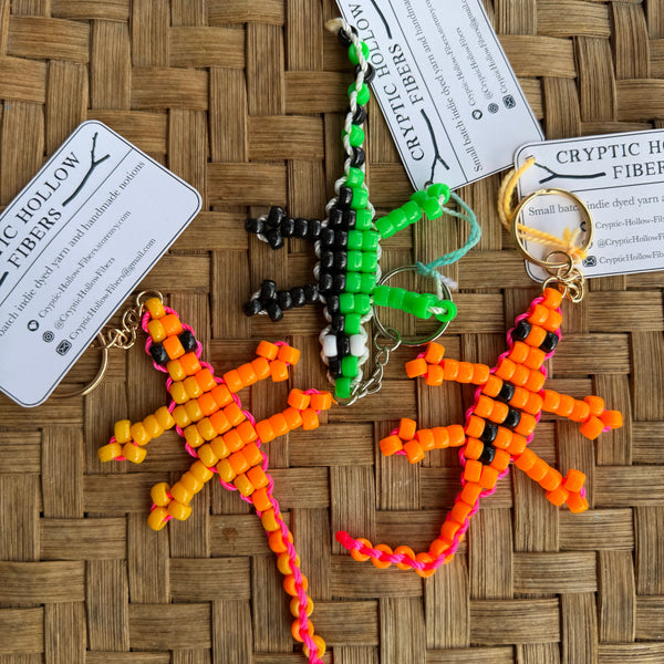 Three beaded lizard keychains on a woven surface with labels.