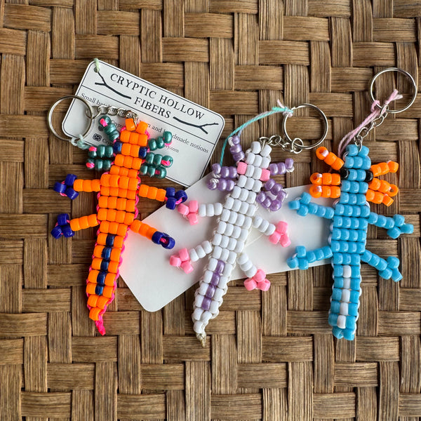 Colorful beaded keychains shaped like axolotls on a woven surface