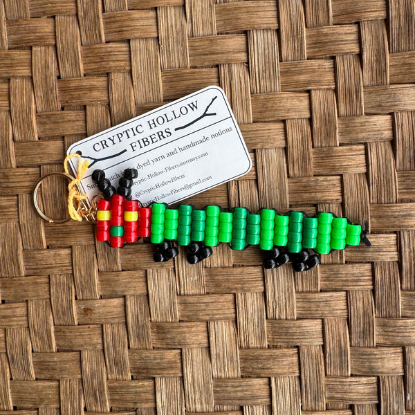 Colorful beaded caterpillar keychain on a woven mat with a business card underneath