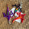 Colorful beaded dragon keychains on a woven surface with visible brand name.