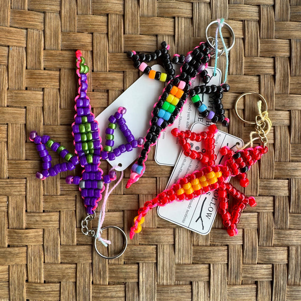 Colorful beaded dragon keychains on a woven surface with visible brand name.