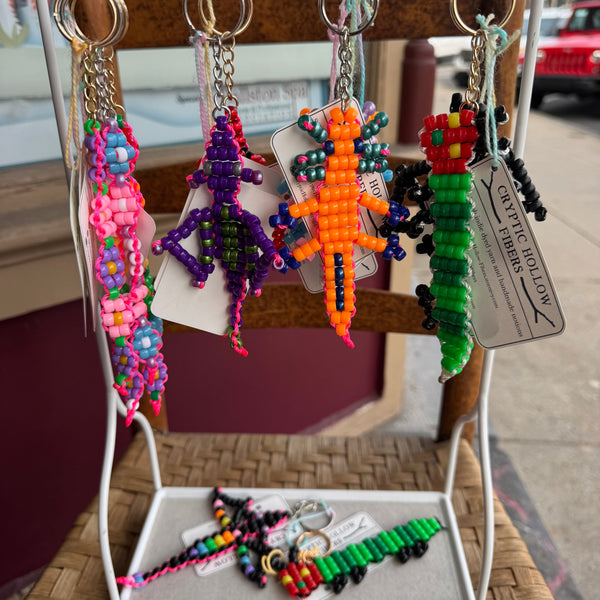 Colorful beaded keychains on a display rack with 'Cryphtic Hollow Fibers' branding.