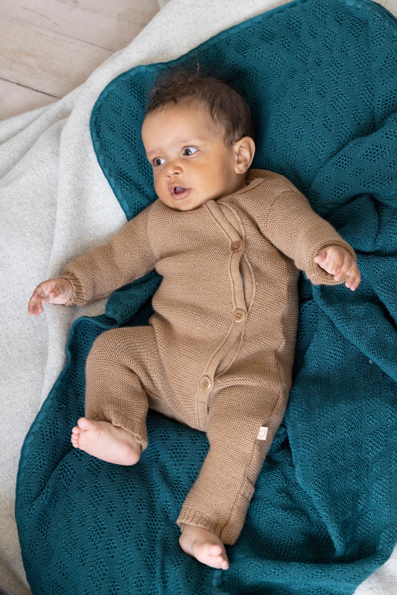 Baby in a brown onesie lying on a teal blanket
