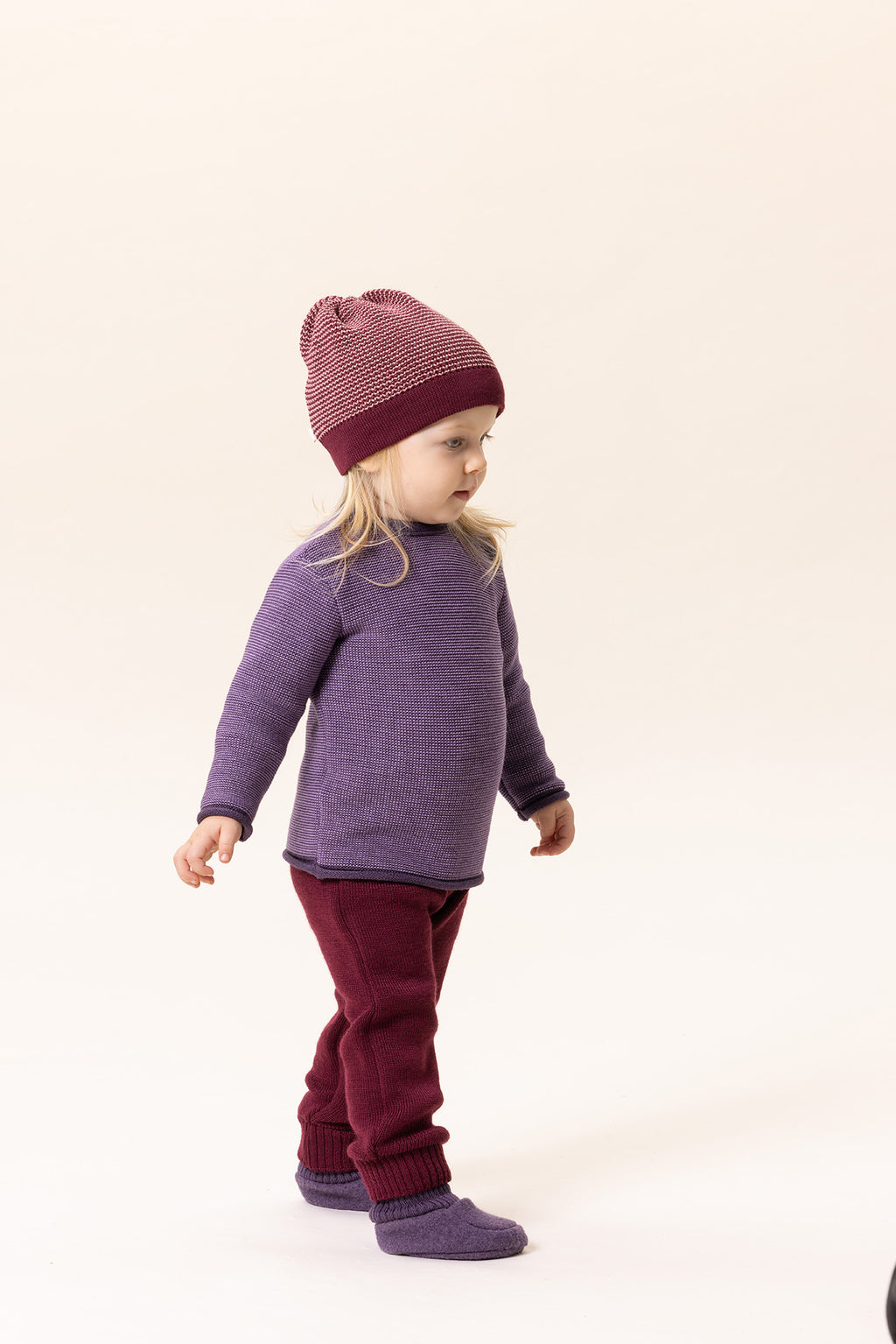 Child wearing a purple sweater and maroon pants with a matching hat on a light background