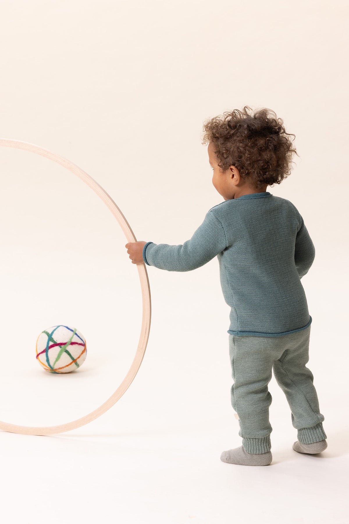 Child playing with a hula hoop and ball on a plain background