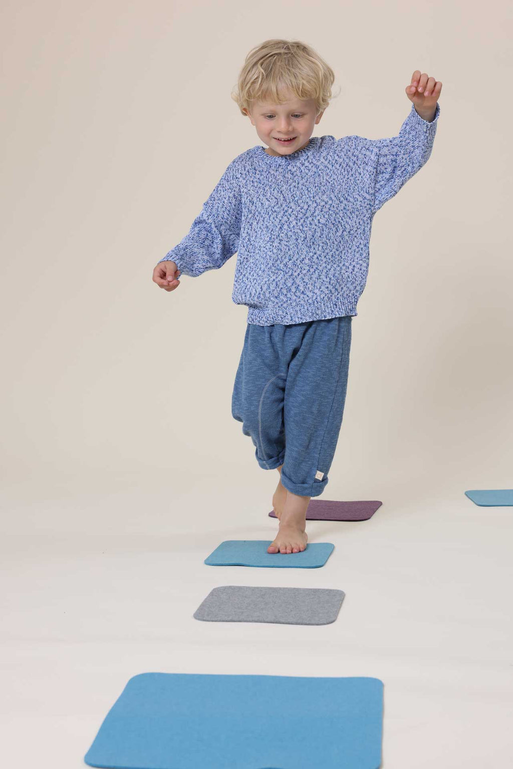 A child wearing a long-sleeve knit sweater with a textured, speckled pattern in blue, white, and subtle pastel tones, shown against a plain off-white background.