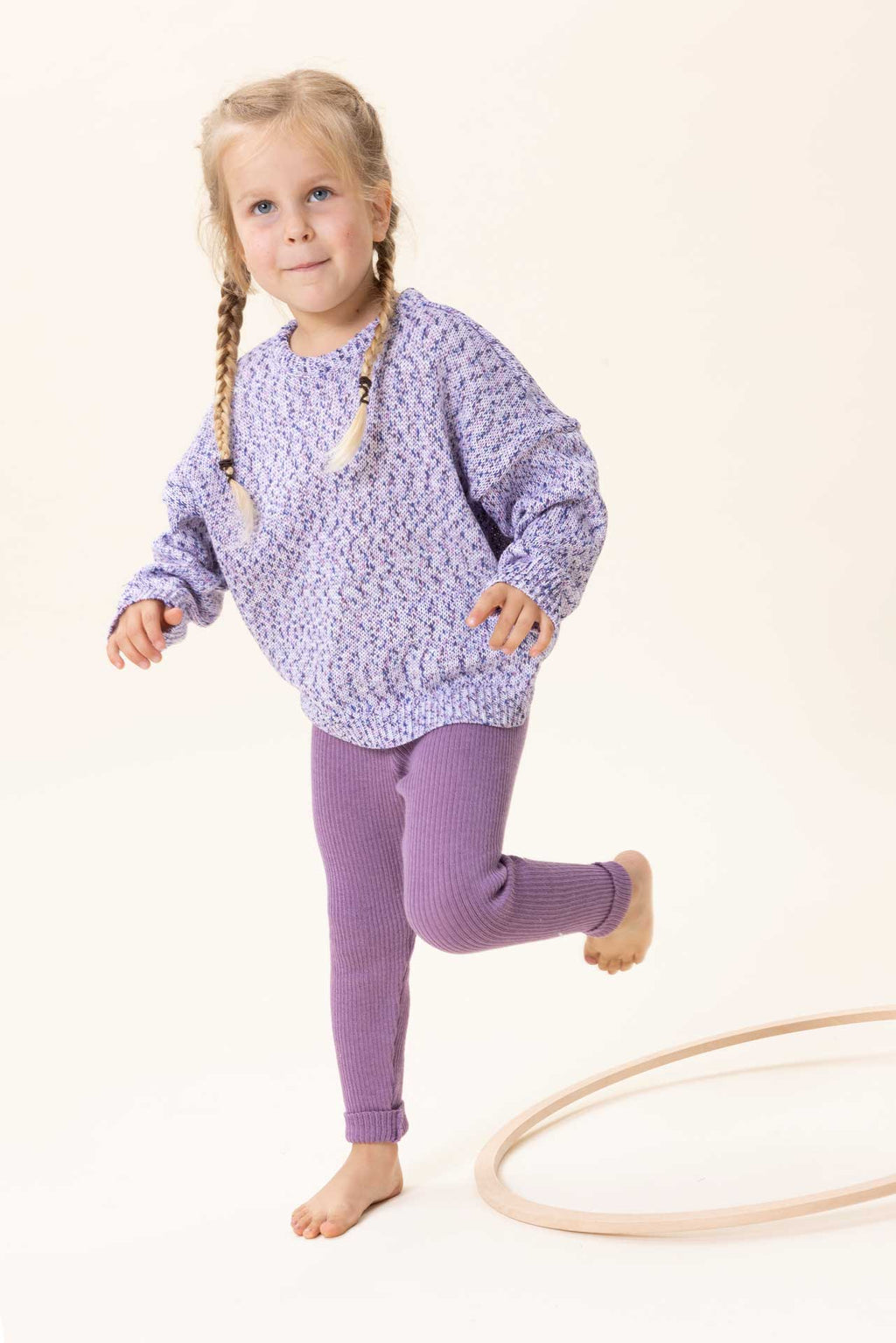 A child wearing a long-sleeve knit sweater with a textured, speckled pattern in purple, white, and subtle pastel tones, shown against a plain off-white background.