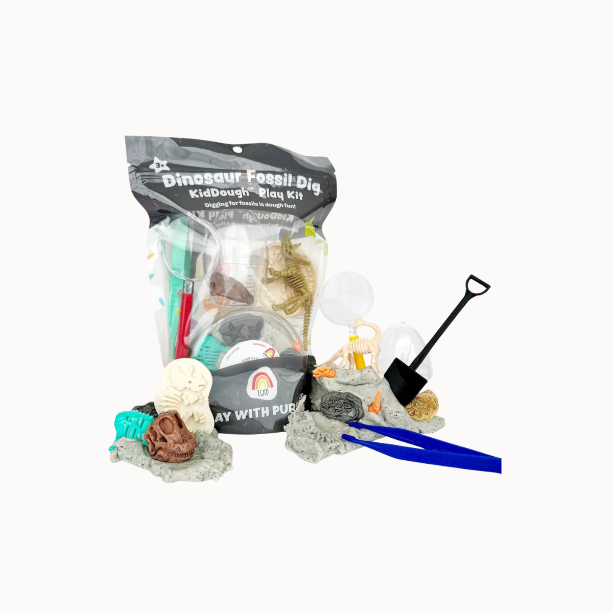 Dinosaur Fossil Dig Kid Dough Play Kit with a black resealable bag containing play dough and accessories, plus several loose items including a black shovel, blue tongs, gray rock pieces, and small toy fossils on a white background.