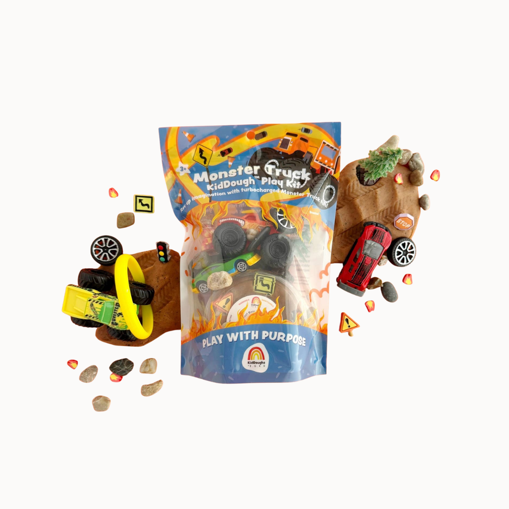 Monster Truck KidDough Play Kit with a blue and orange bag of dough and various toy vehicles and road elements scattered around on a white background.
