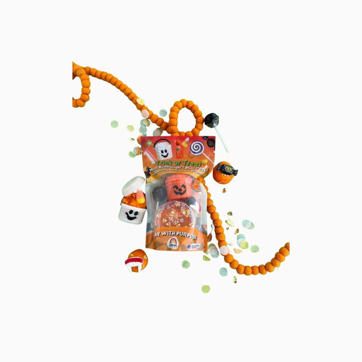A Halloween-themed candy bag with orange beaded string, floating marshmallows, a jack-o'-lantern candy, and confetti on a plain white background.