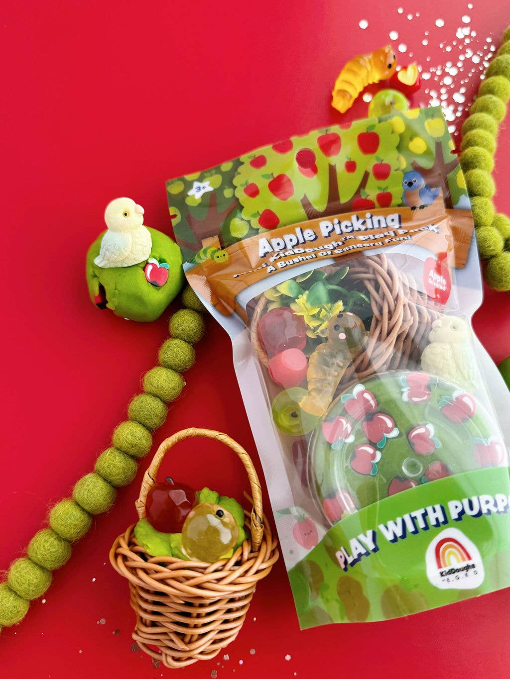 Toy set with green apple-shaped toy, basket, and packaging on a red background