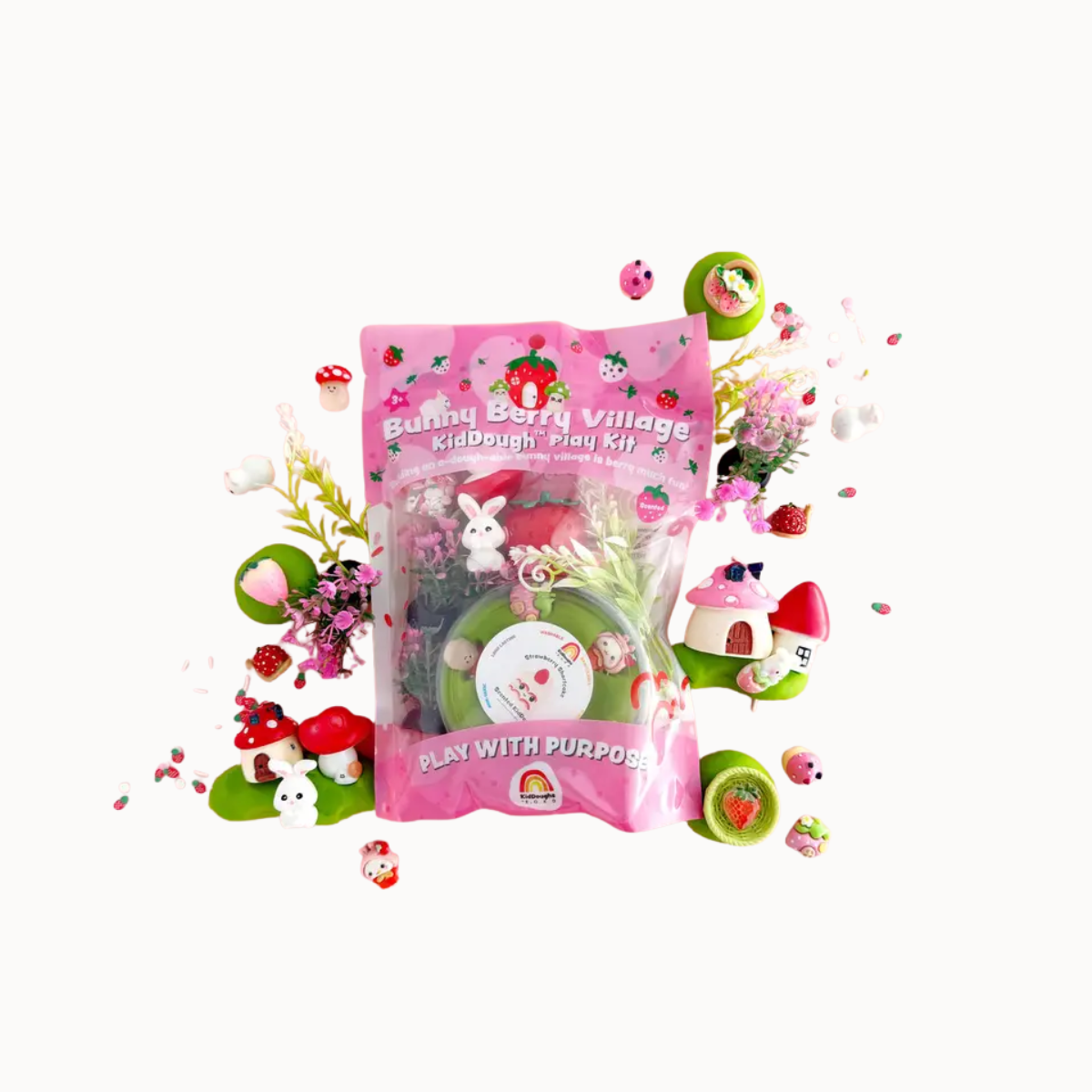 A pink 'Bunny Berry Village Kid's Dough Play Kit' bag surrounded by decorative craft elements like mini mushroom houses, kiwi slices, and small figurines on a plain white background.