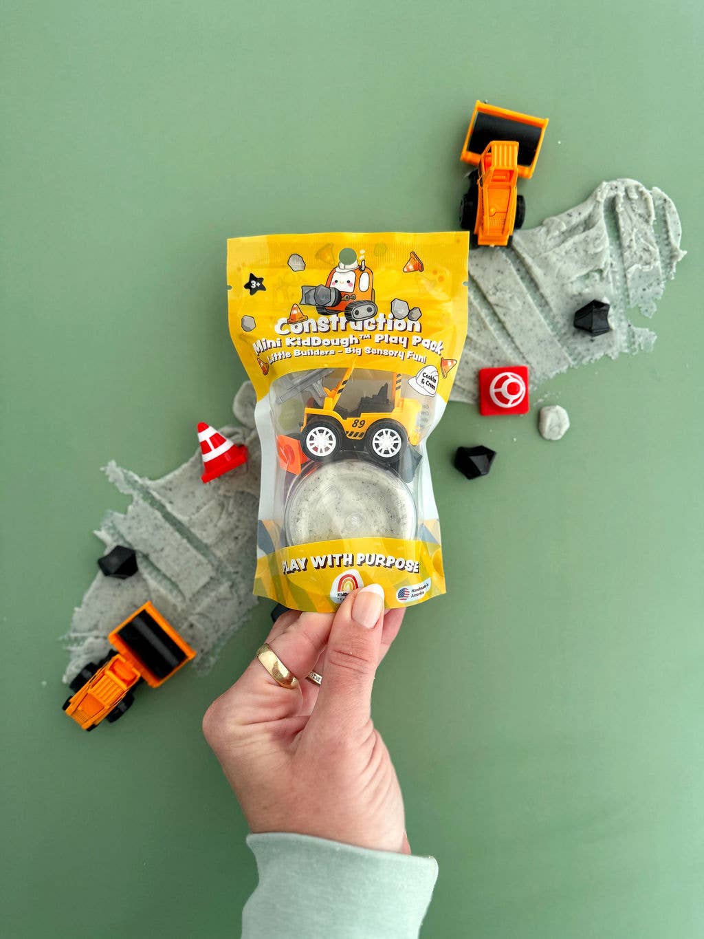 Hand holding a construction-themed play set with a green background