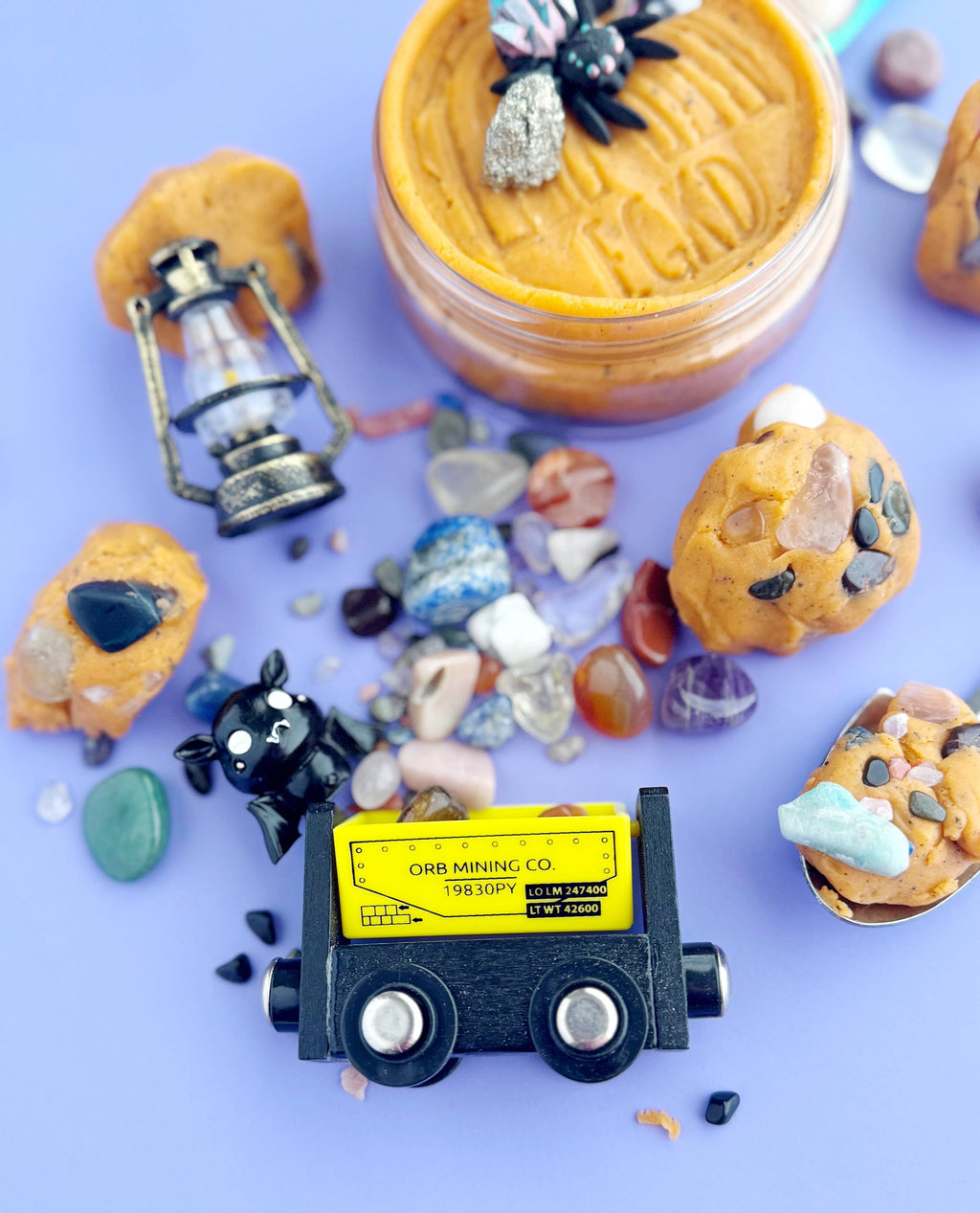Miniature mining truck surrounded by small rocks and a jar of what appears to be peanut butter on a purple background.